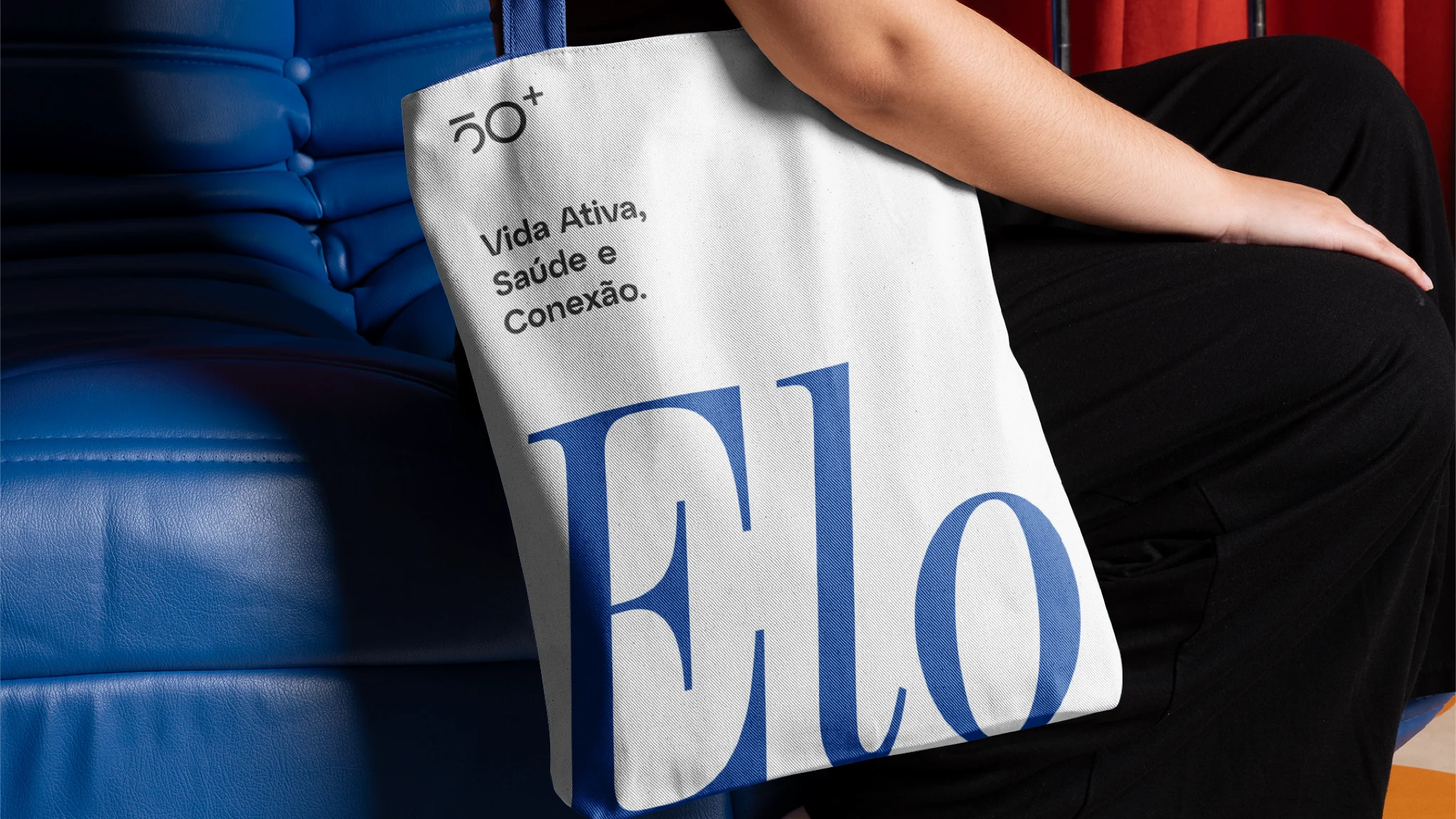 Capa Elo 50+: bolsa com identidade visual sobre sofá azul